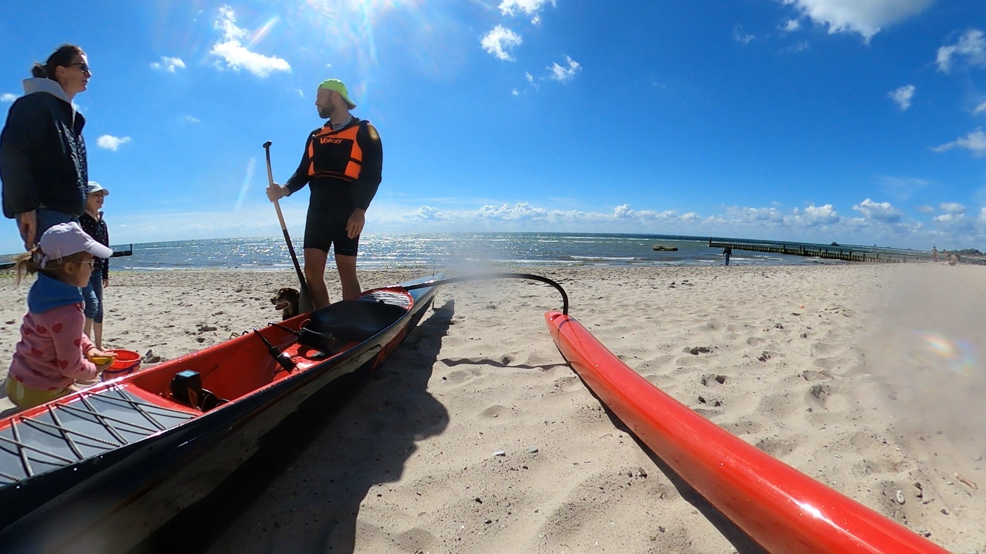 Hannes Wagner steht mit Paddel am Sandstrand, daneben liegen ein Surfski und ein Outrigger-Kanu.